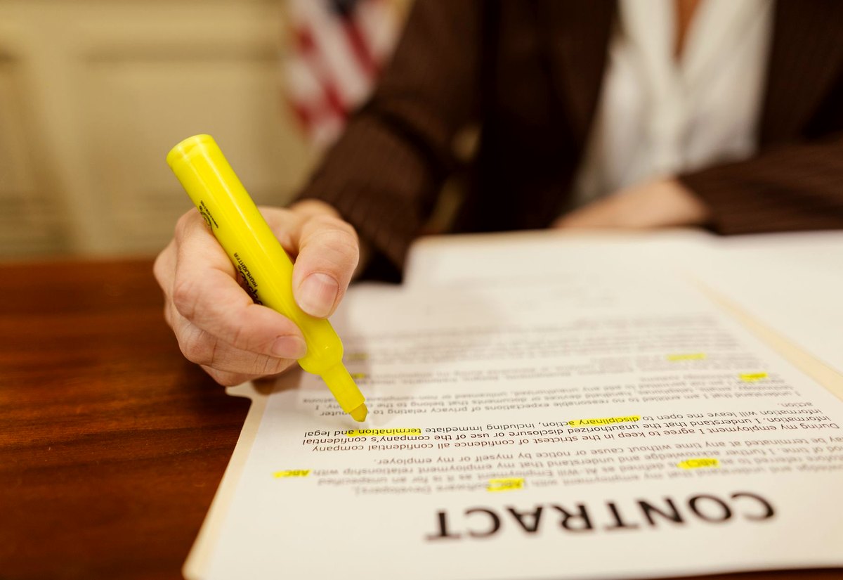 Mão com marca-texto amarelo destacando cláusulas de um contrato impresso