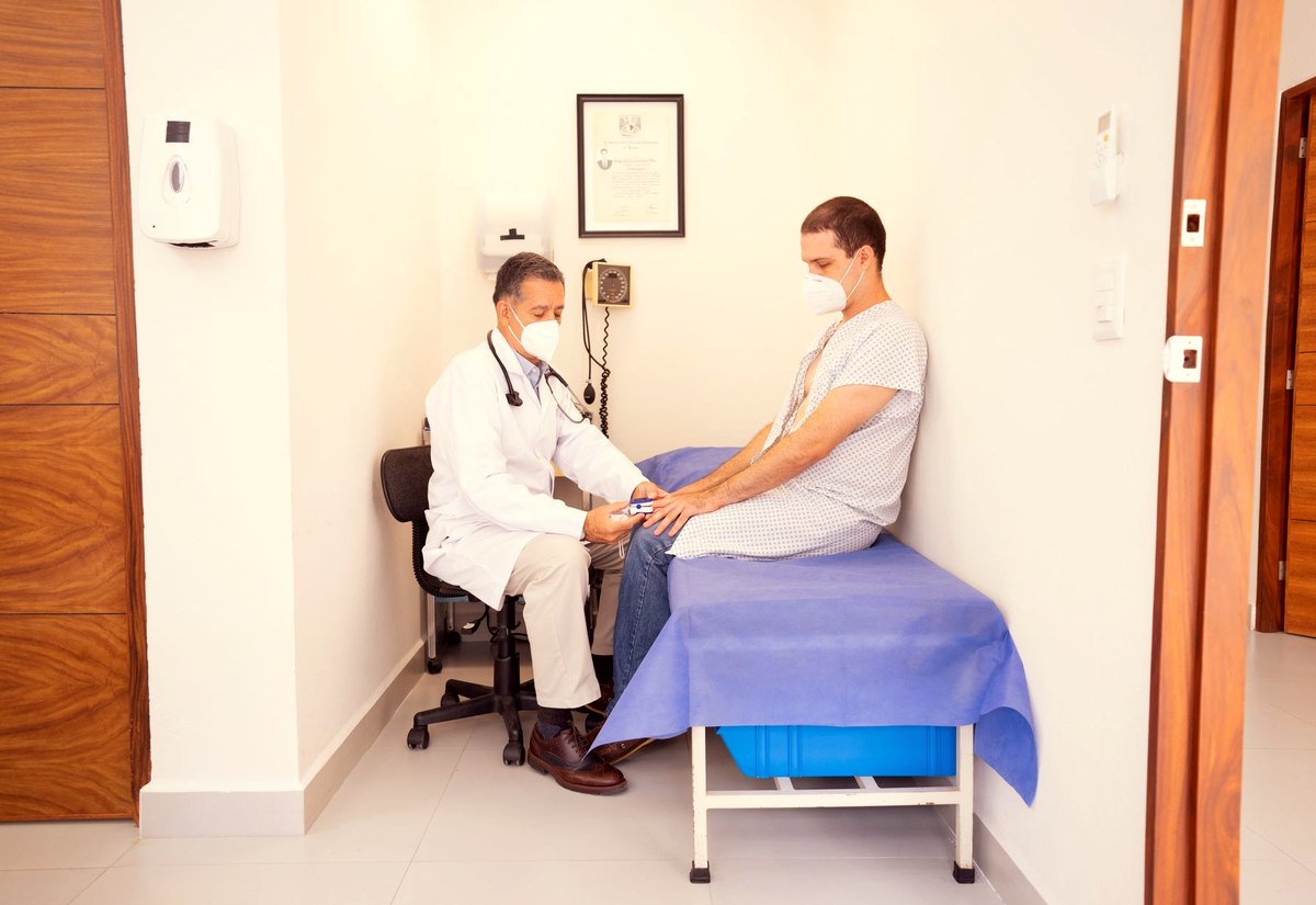 Médico examinando o joelho de um paciente sentado na maca do consultório