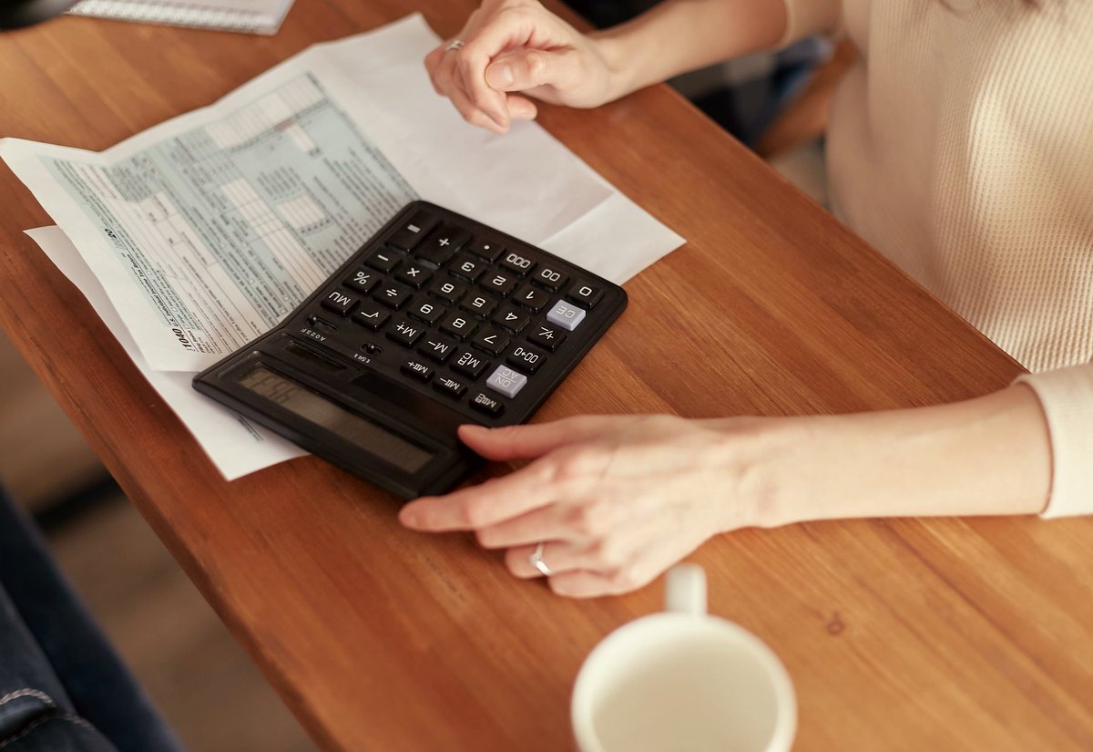 Mãos sobre a mesa de madeira usando calculadora ao lado de documentos e uma xícara