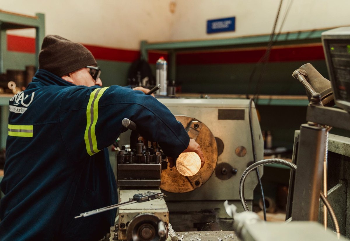 Operário de gorro e óculos de proteção trabalha num torno de metal numa oficina industrial