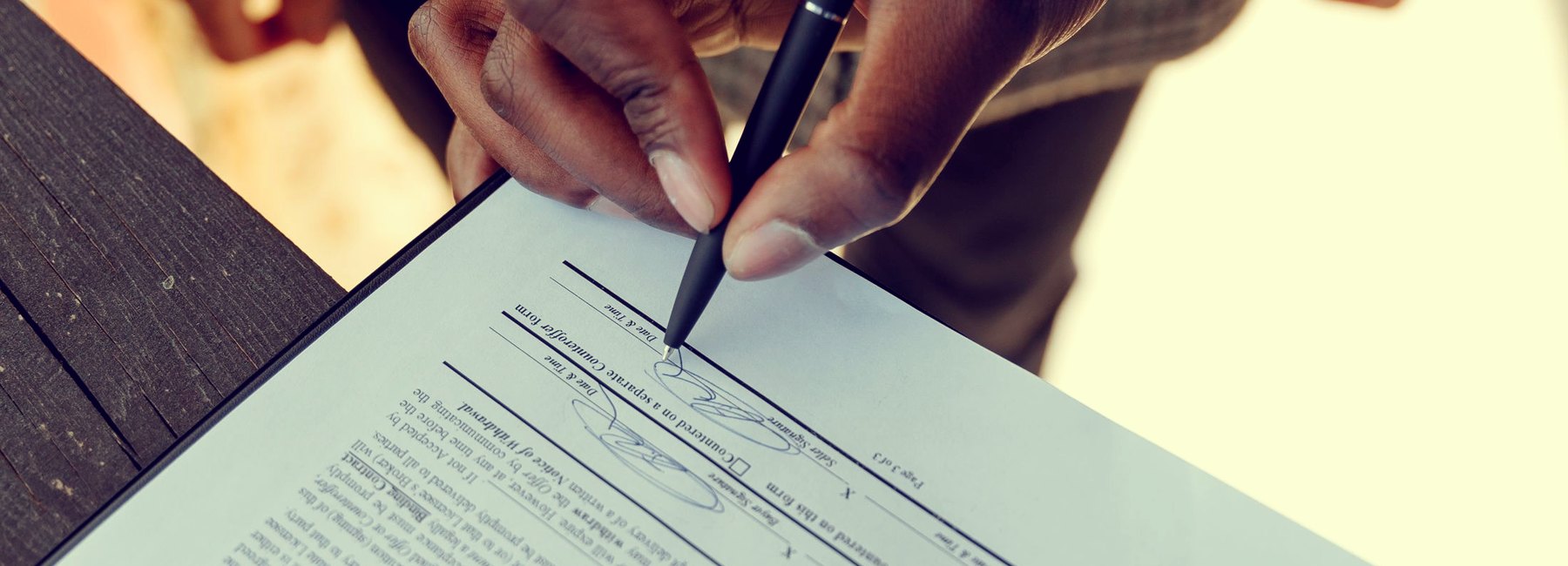 Mão assinando um contrato com caneta sobre a prancheta