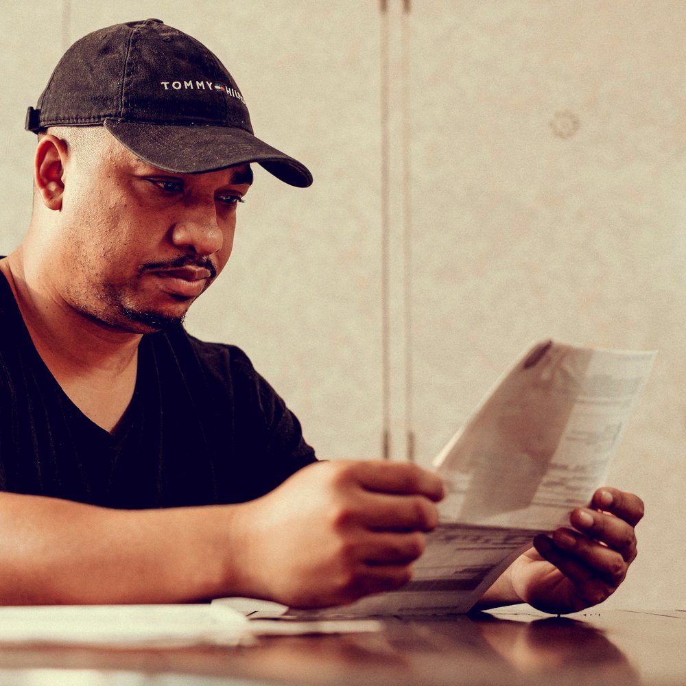 Homem de boné lê um documento à mesa, com expressão séria