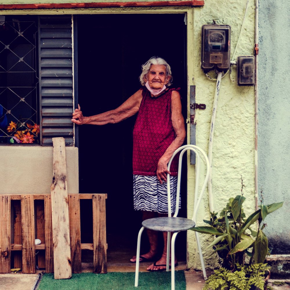 Senhora idosa na porta de casa, apoiada na cadeira